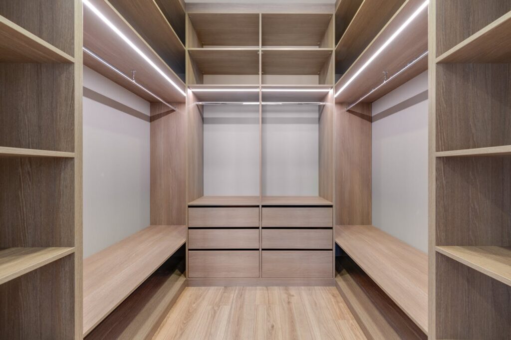 Spacious walk-in closet with wooden shelves and LED lighting creates a minimalist and modern design.